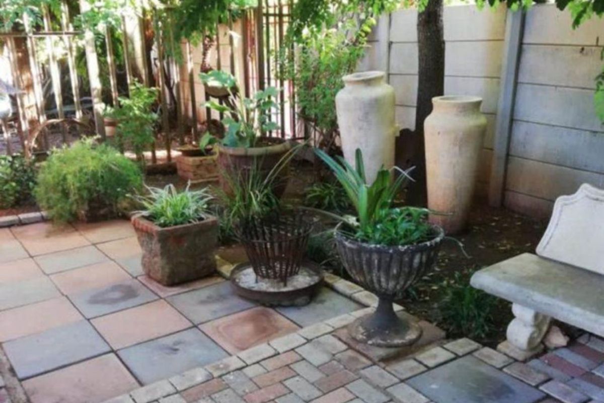 A paved rear courtyard area featuring a mix of brick and tile paving, enclosed by a precast concrete wall and metal fencing.