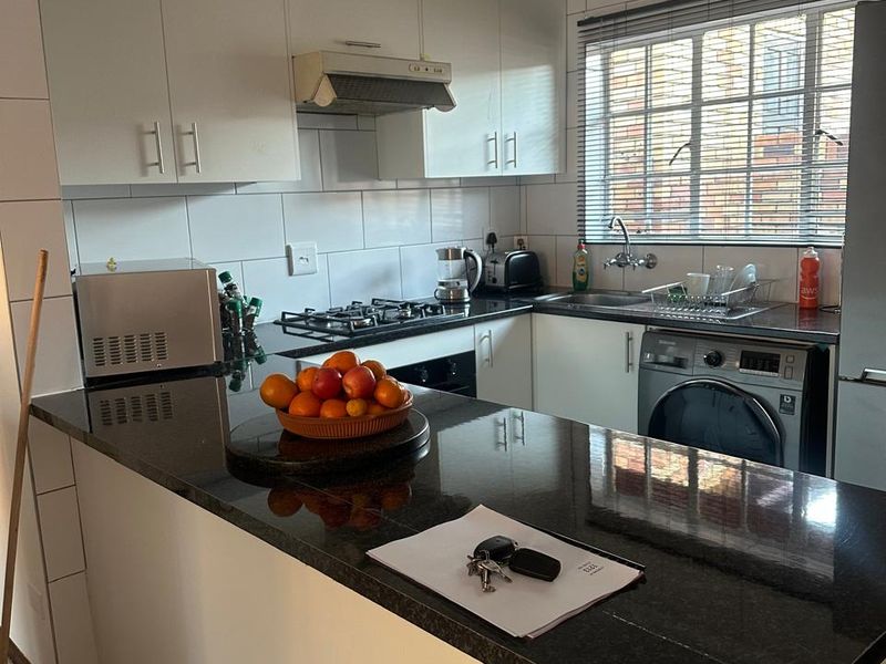 A functional kitchen featuring white cabinetry, dark granite countertops, a gas hob, and integrated laundry plumbing.