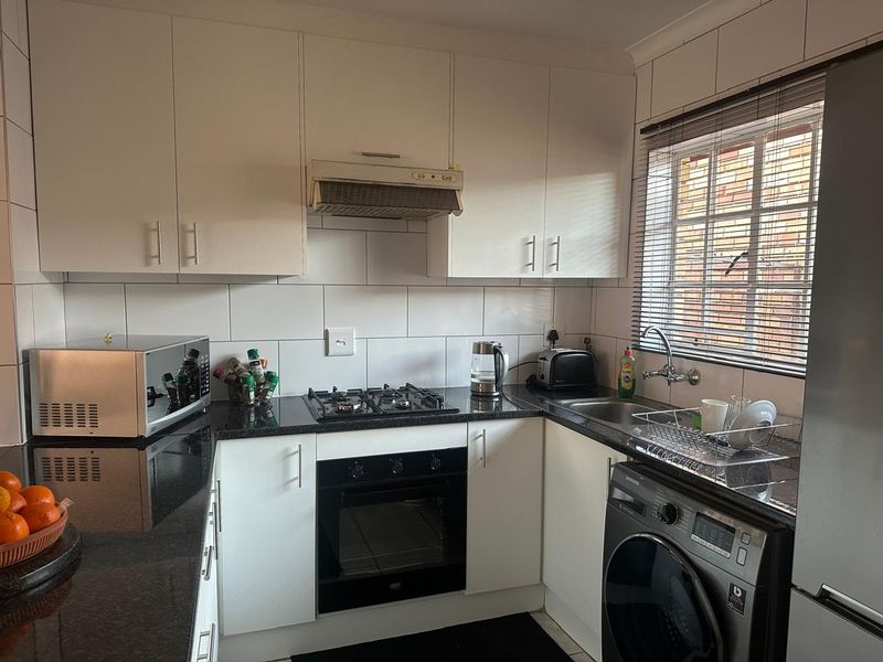 A functional kitchen featuring white cabinetry, dark granite countertops, a gas hob, built-in oven, and a tiled backsplash with a window view.