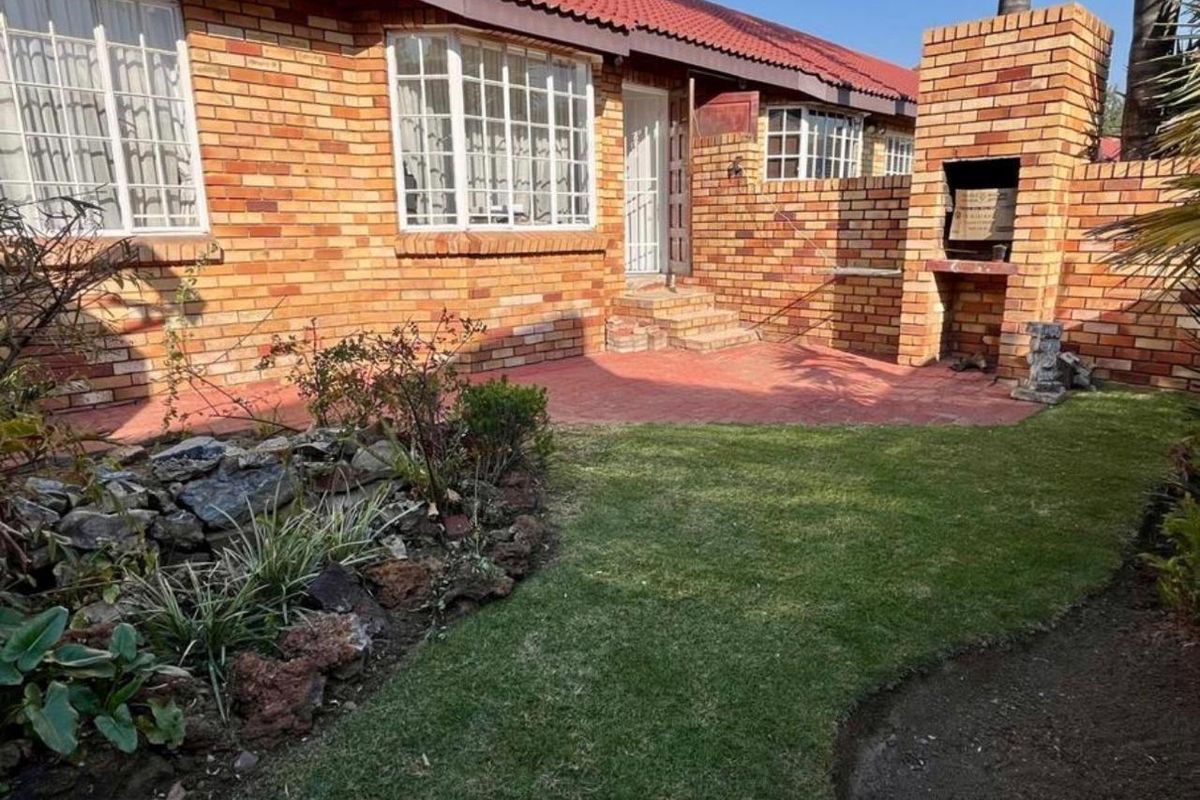 Rear exterior view of the townhouse featuring a brick facade, tiled roof, paved patio area, and a built-in brick braai in the garden.