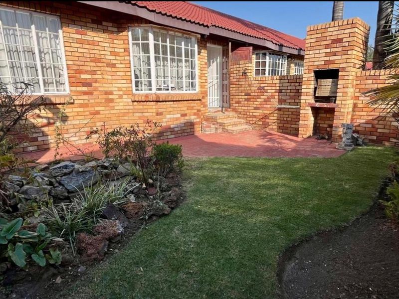 Rear exterior view of the townhouse featuring a brick facade, tiled roof, paved patio area, and a built-in brick braai in the garden.
