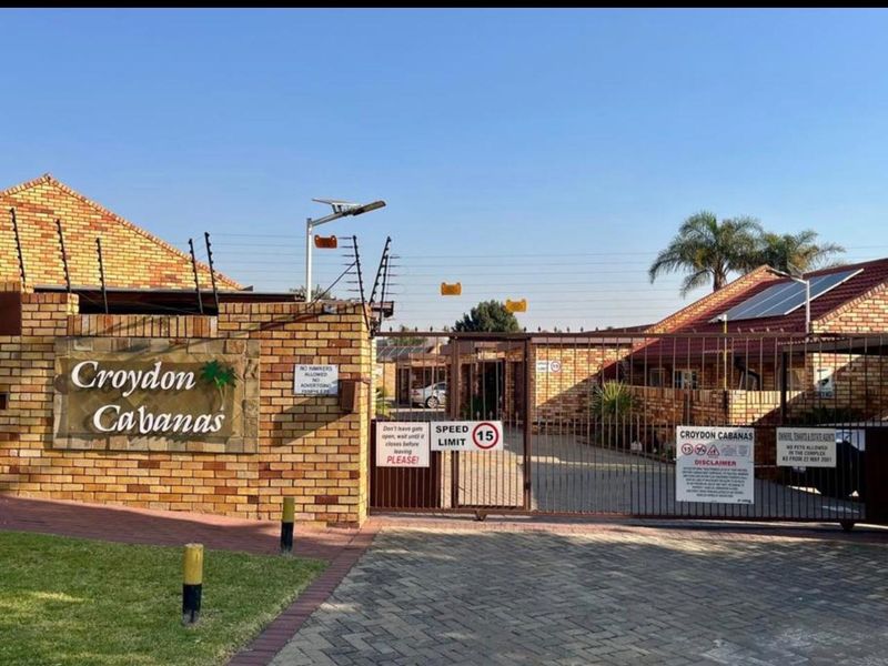 The entrance to Croydon Cabanas featuring a brick boundary wall, electric fencing, and a secure metal gate access point.