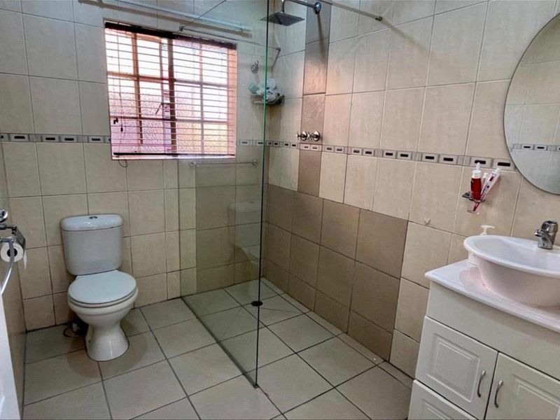 A functional bathroom featuring a walk-in shower with a glass screen, a vanity with a vessel sink, and neutral wall and floor tiling.