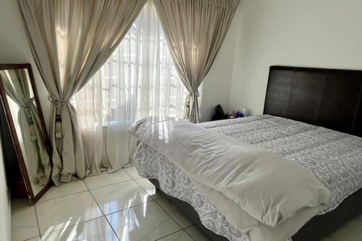 A bedroom featuring tiled flooring and large windows with curtain rails, providing natural light.