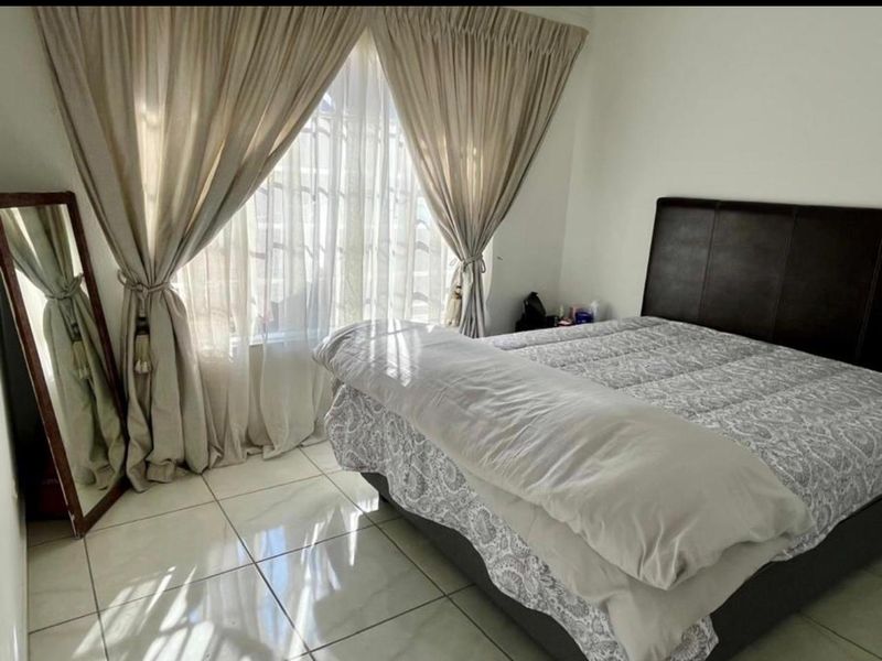 A bedroom featuring tiled flooring and large windows with curtain rails, providing natural light.