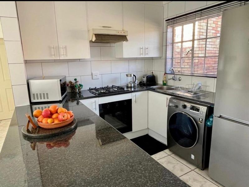 Compact kitchen featuring granite countertops, white cabinetry, built-in oven with gas hob, and integrated laundry plumbing.
