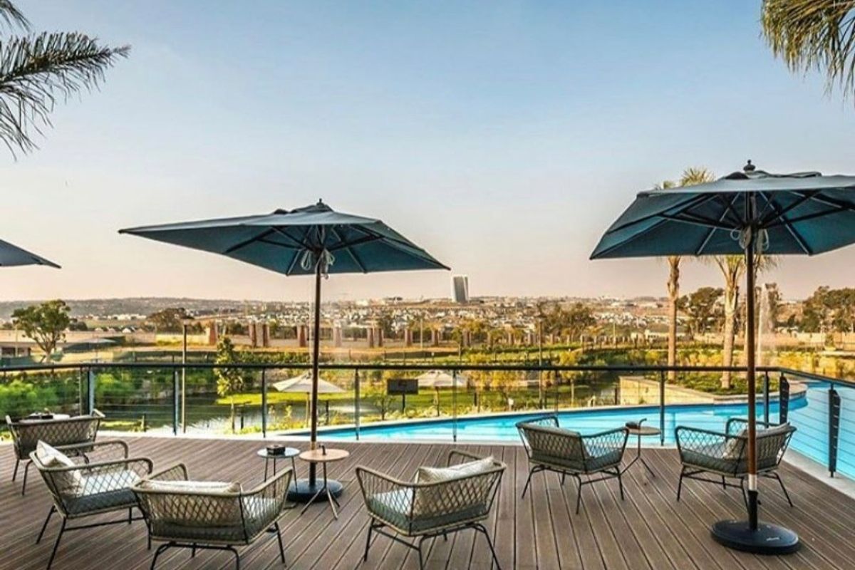 An elevated outdoor pool area featuring modern timber decking, a glass balustrade, and expansive views over the surrounding landscape.
