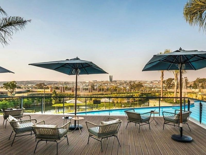 An elevated outdoor pool area featuring modern timber decking, a glass balustrade, and expansive views over the surrounding landscape.