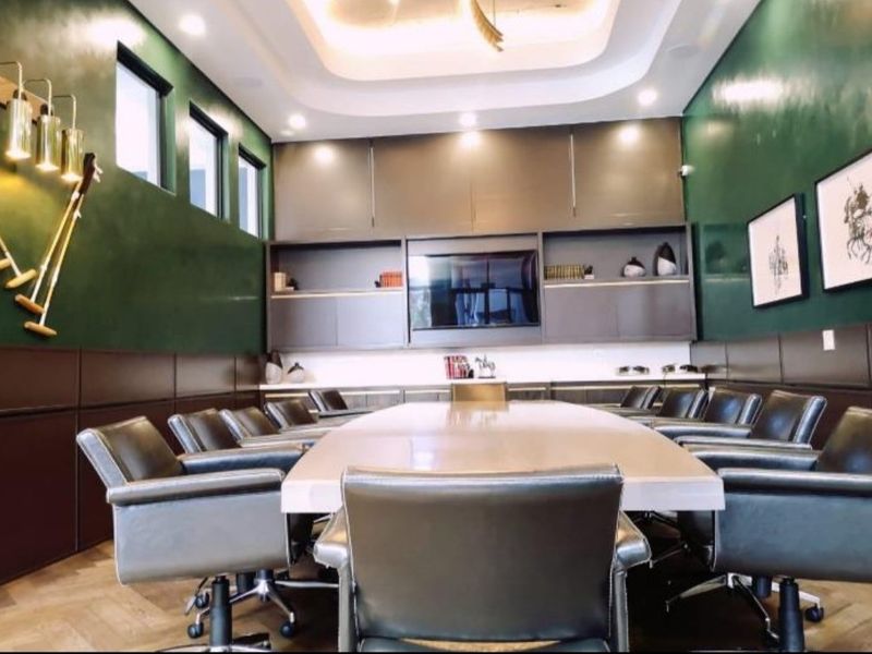 A professional boardroom featuring dark green wall paneling, custom built-in cabinetry, a coffered ceiling with recessed lighting, and elegant herringbone flooring.