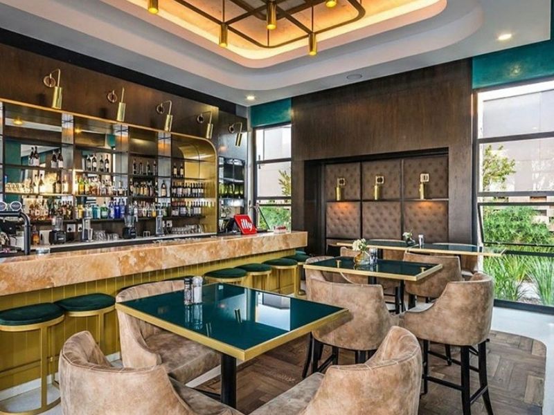 A sophisticated, well-appointed bar area featuring a stone-topped counter, mirrored back bar, elegant coffered ceiling with recessed lighting, and high-quality parquet flooring.