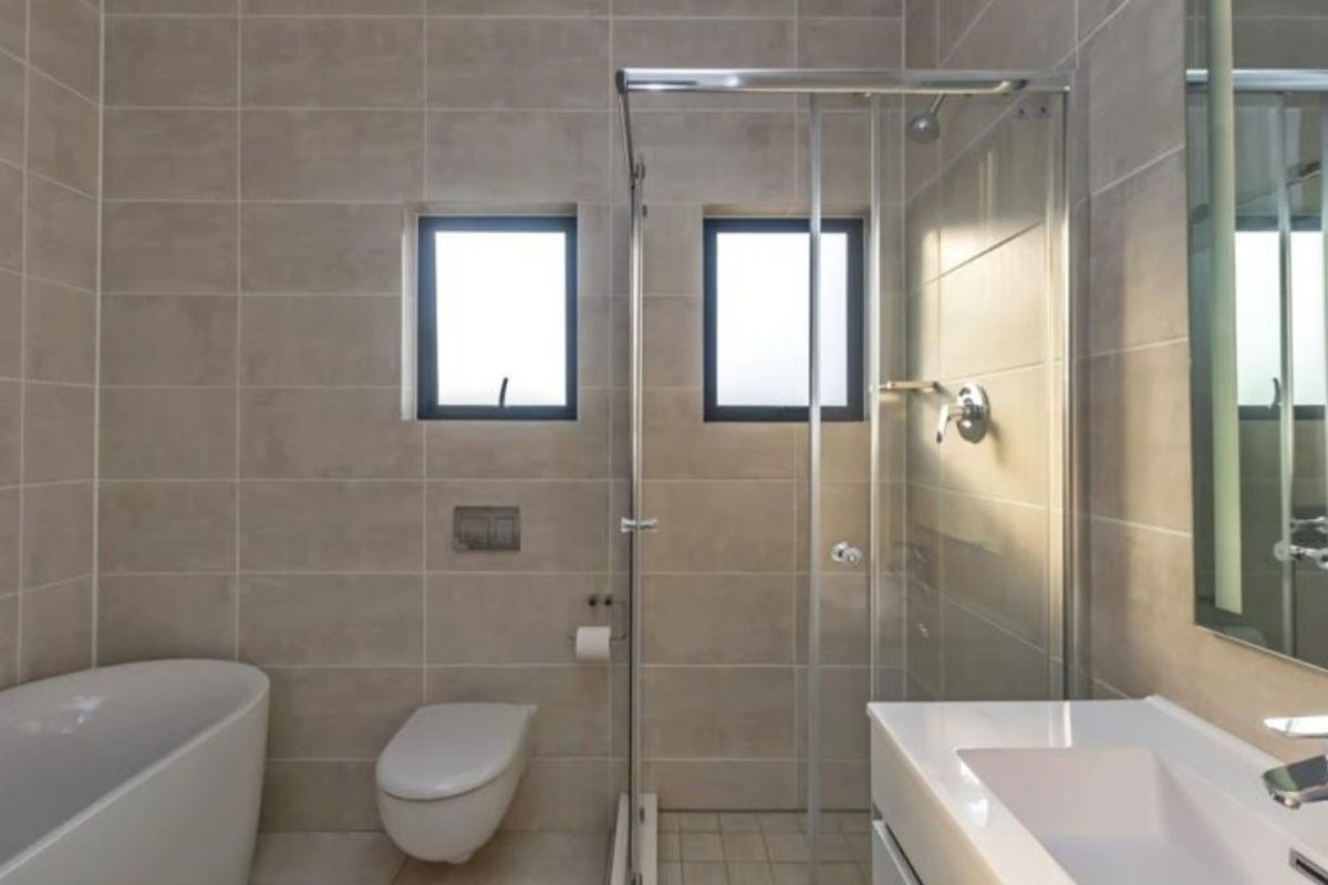 Modern bathroom featuring a freestanding bathtub, glass-enclosed shower, wall-mounted toilet, and a sleek vanity basin with neutral wall tiling.