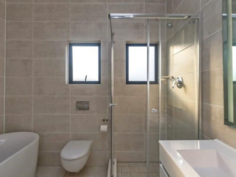 Modern bathroom featuring a freestanding bathtub, glass-enclosed shower, wall-mounted toilet, and a sleek vanity basin with neutral wall tiling.