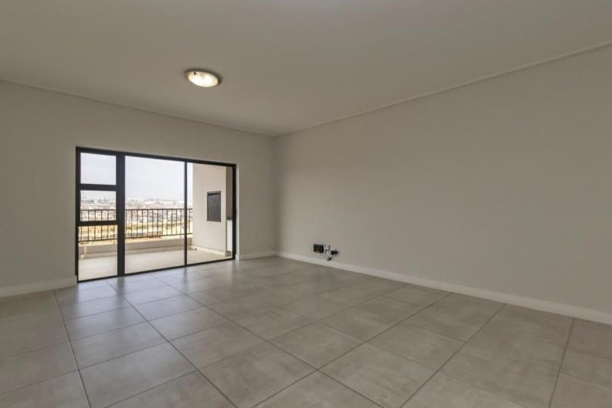 A spacious, empty living area featuring neutral tiled flooring and a large sliding glass door providing access to an outdoor balcony.