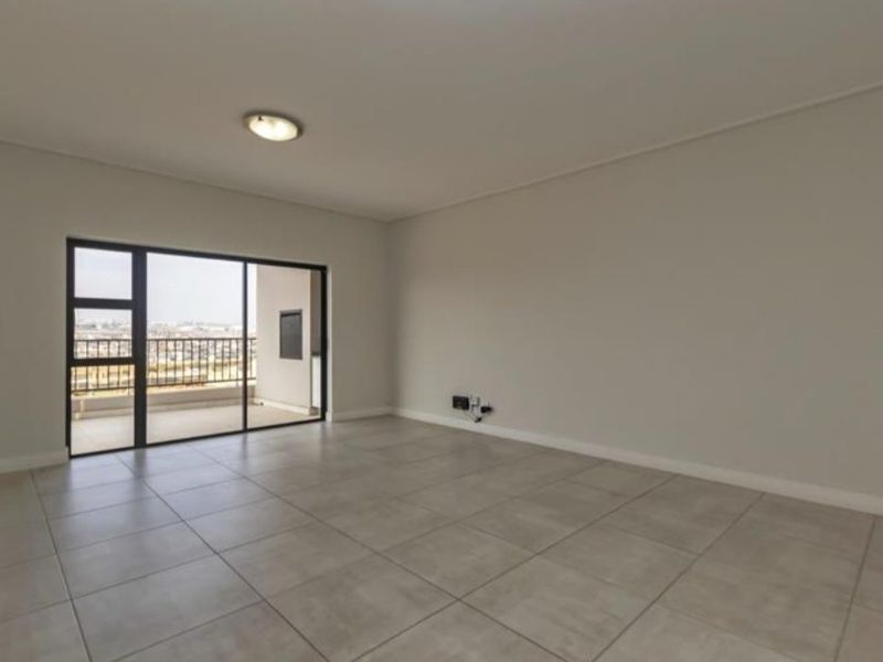 A spacious, empty living area featuring neutral tiled flooring and a large sliding glass door providing access to an outdoor balcony.