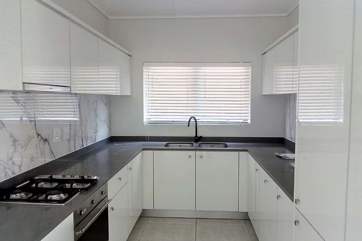 Modern galley-style kitchen featuring white high-gloss cabinetry, dark stone countertops, marble-look splashback, integrated gas hob, and built-in oven.
