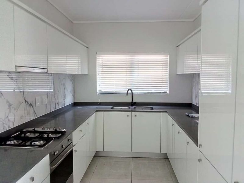 Modern galley-style kitchen featuring white high-gloss cabinetry, dark stone countertops, marble-look splashback, integrated gas hob, and built-in oven.