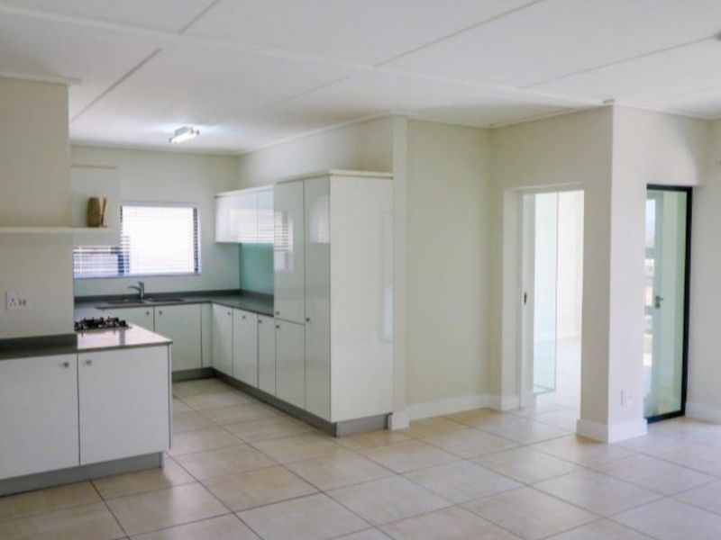 A bright open-plan living and kitchen area featuring modern white cabinetry, a gas hob, tiled flooring, and access to an outdoor balcony.