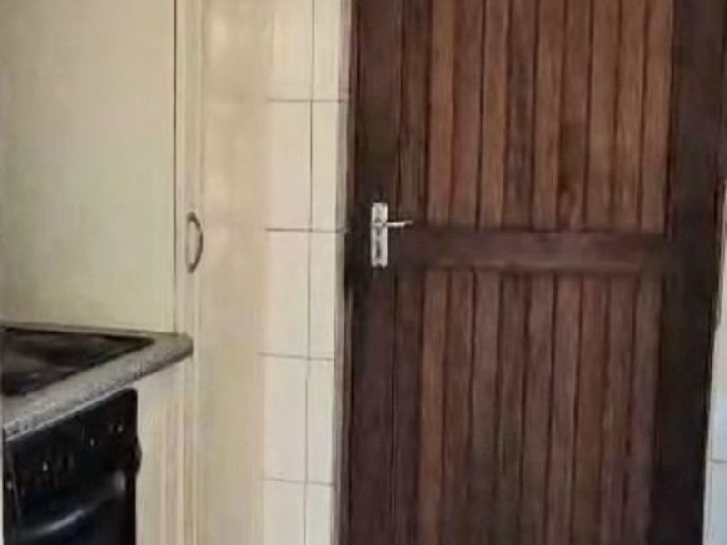 A compact kitchen area featuring built-in cabinetry, an integrated oven, extractor fan, and tiled flooring, presenting an opportunity for modern renovation.