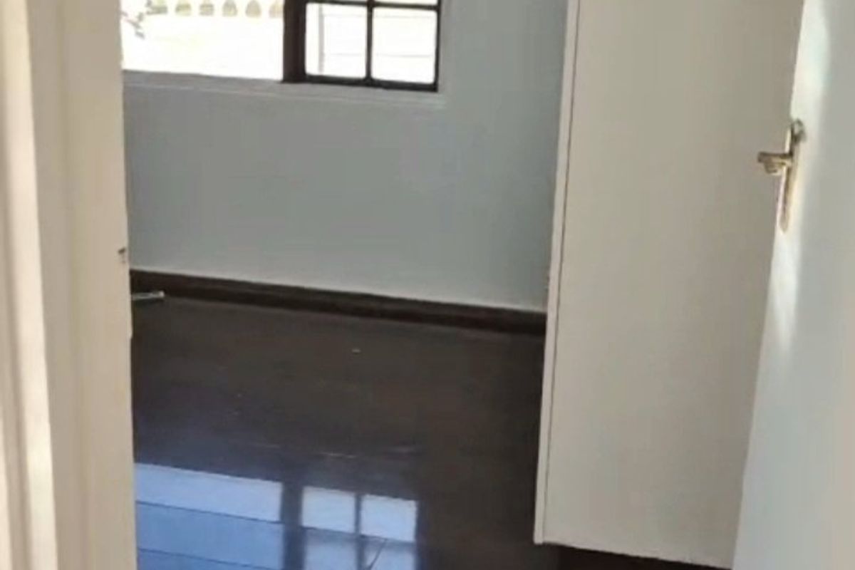 A bright, empty bedroom featuring dark laminate flooring, a built-in cupboard, and a window with grid detailing.