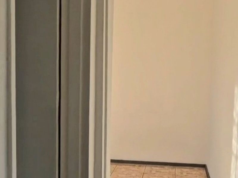 A view through a doorway into an empty, tiled hallway with neutral walls and natural light.