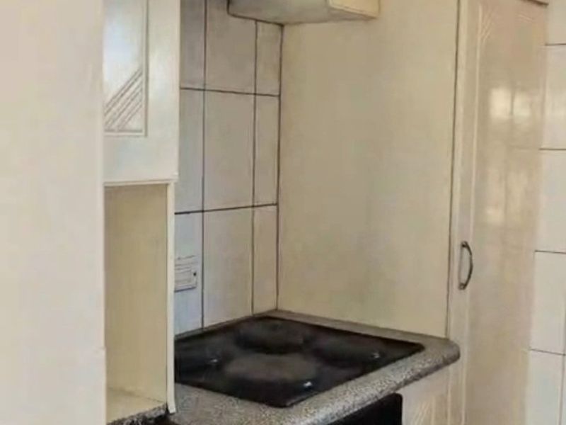 A compact kitchen featuring built-in cabinetry, an electric hob, an oven, and an extractor fan with a tiled backsplash.