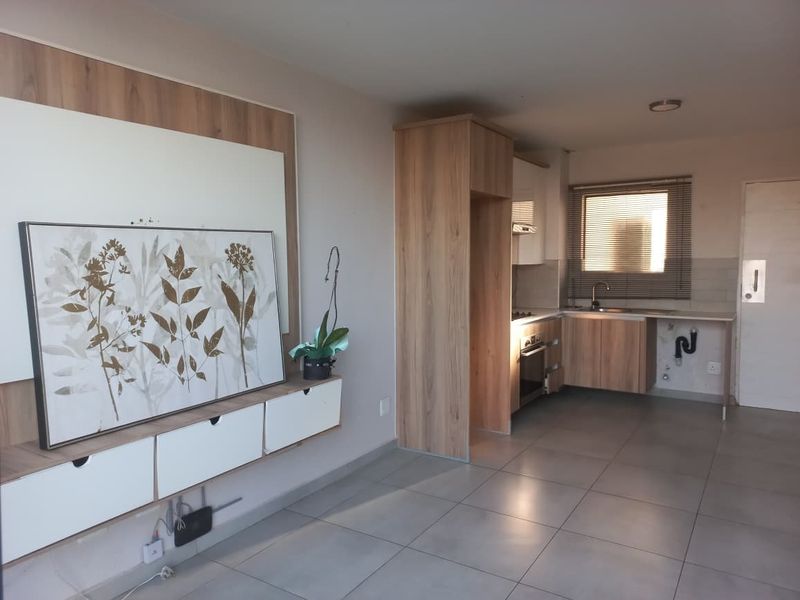 Open-plan living area featuring a modern kitchen with wood-finish cabinetry, tiled floors, and a built-in media console in the lounge section.
