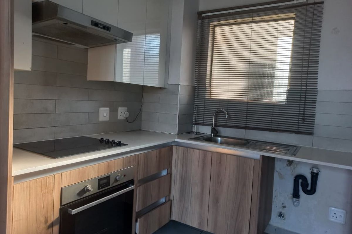 A compact kitchen featuring modern laminate cabinetry, a built-in oven, electric hob, and tiled backsplash, requiring minor repairs to the exposed plumbing area.