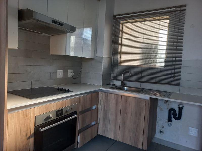 A compact kitchen featuring modern laminate cabinetry, a built-in oven, electric hob, and tiled backsplash, requiring minor repairs to the exposed plumbing area.