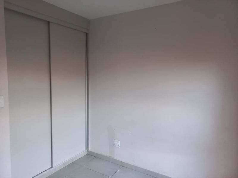 A clean, empty bedroom featuring neutral walls, tiled flooring, and a built-in sliding door wardrobe.