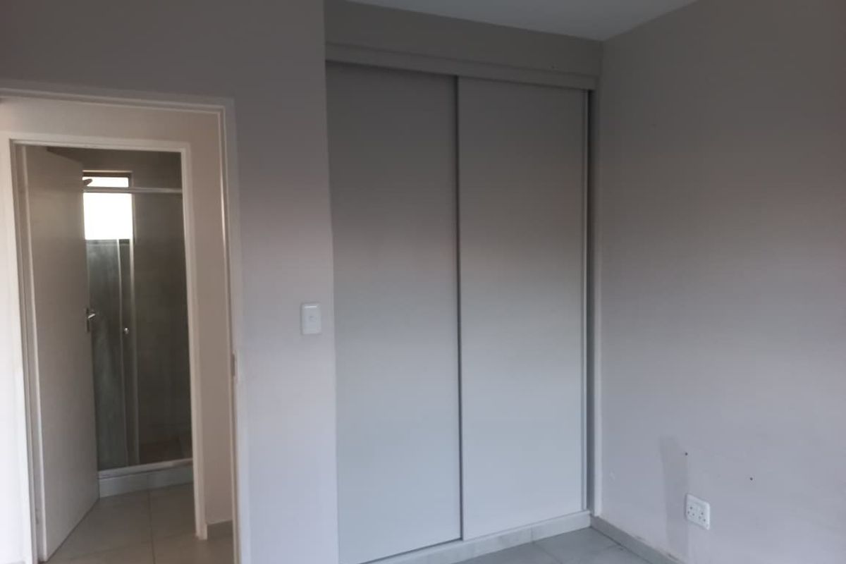A clean, neutral-toned bedroom featuring built-in sliding door wardrobes and direct access to an en-suite bathroom with tiled flooring throughout.