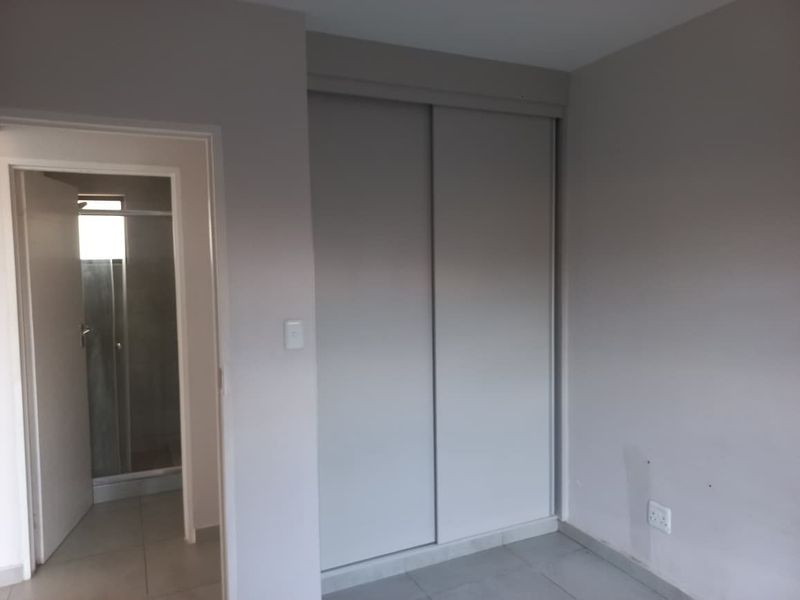A clean, neutral-toned bedroom featuring built-in sliding door wardrobes and direct access to an en-suite bathroom with tiled flooring throughout.