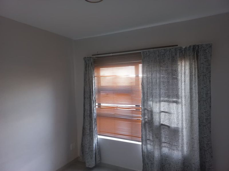 A neutral-toned bedroom featuring a window fitted with venetian blinds and curtain tracks, offering a blank canvas for interior design.