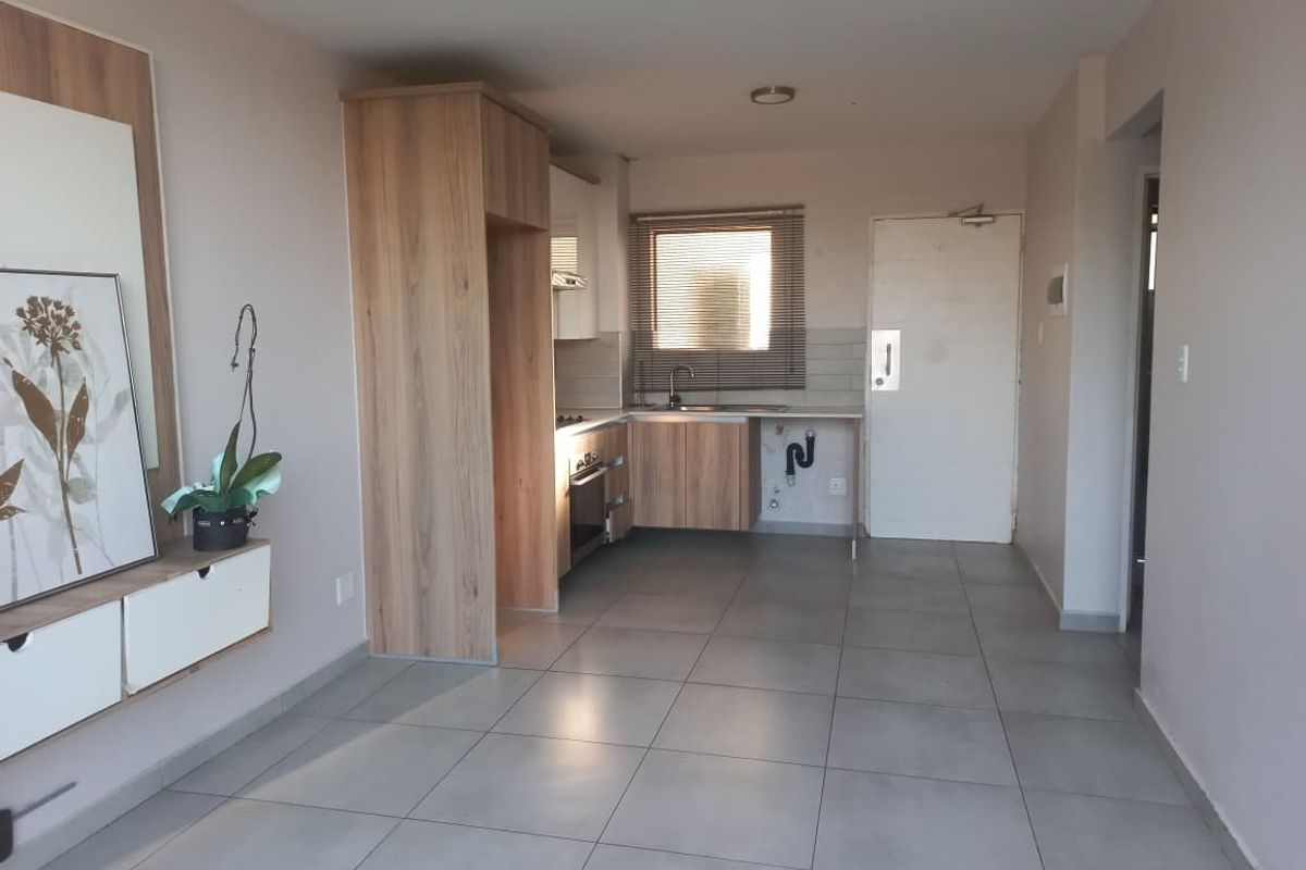 Open-plan living area featuring a compact kitchen with built-in cabinetry, oven, and tiled flooring throughout.