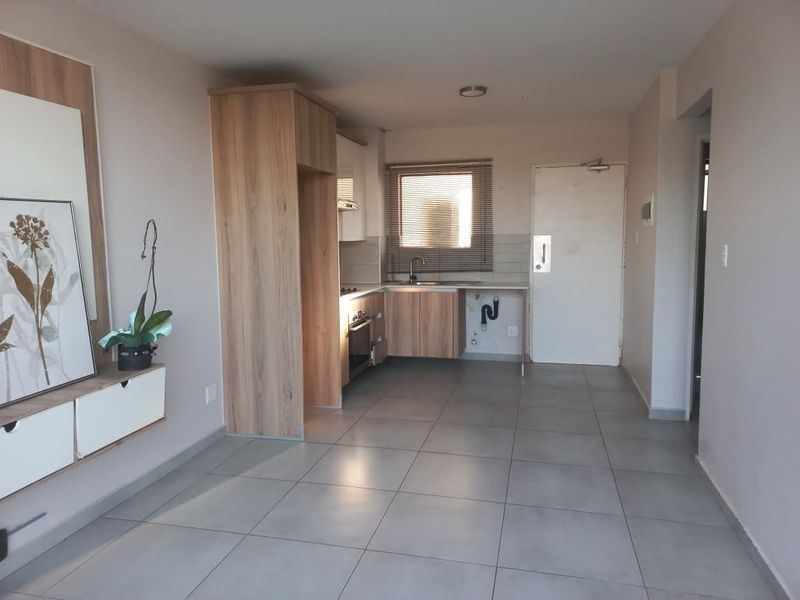Open-plan living area featuring a compact kitchen with built-in cabinetry, oven, and tiled flooring throughout.