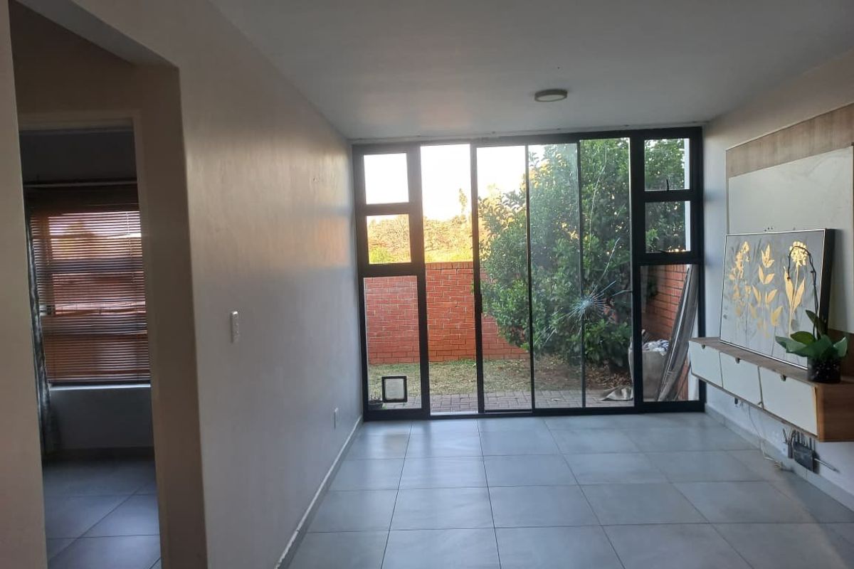 Living room featuring large sliding glass doors with a cracked pane, tiled flooring, and a built-in media console, offering direct access to the rear garden.