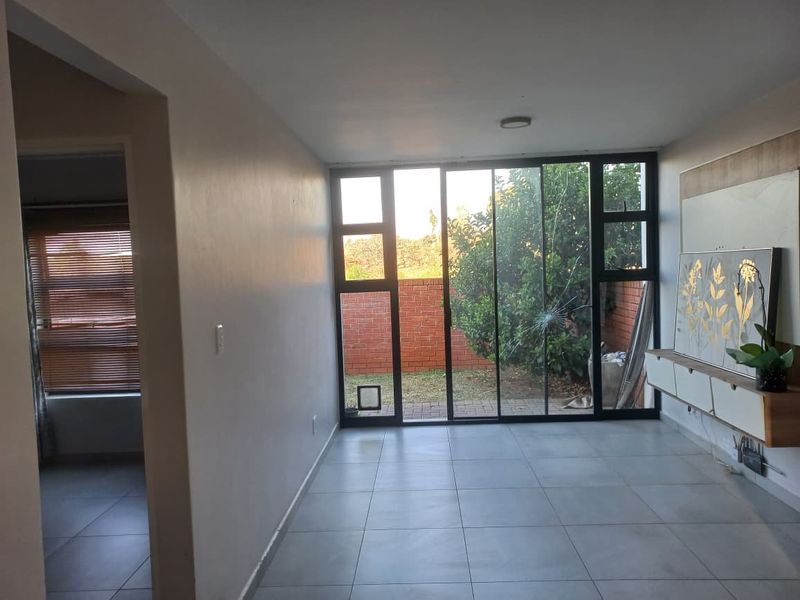 Living room featuring large sliding glass doors with a cracked pane, tiled flooring, and a built-in media console, offering direct access to the rear garden.