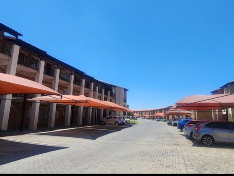 Exterior view of an apartment complex featuring paved parking areas with shade cloth carports and multi-story residential buildings.