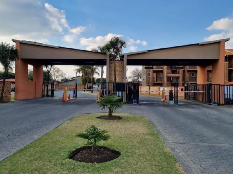 The main entrance to the apartment complex featuring a secure boom gate access system and a well-maintained paved driveway.