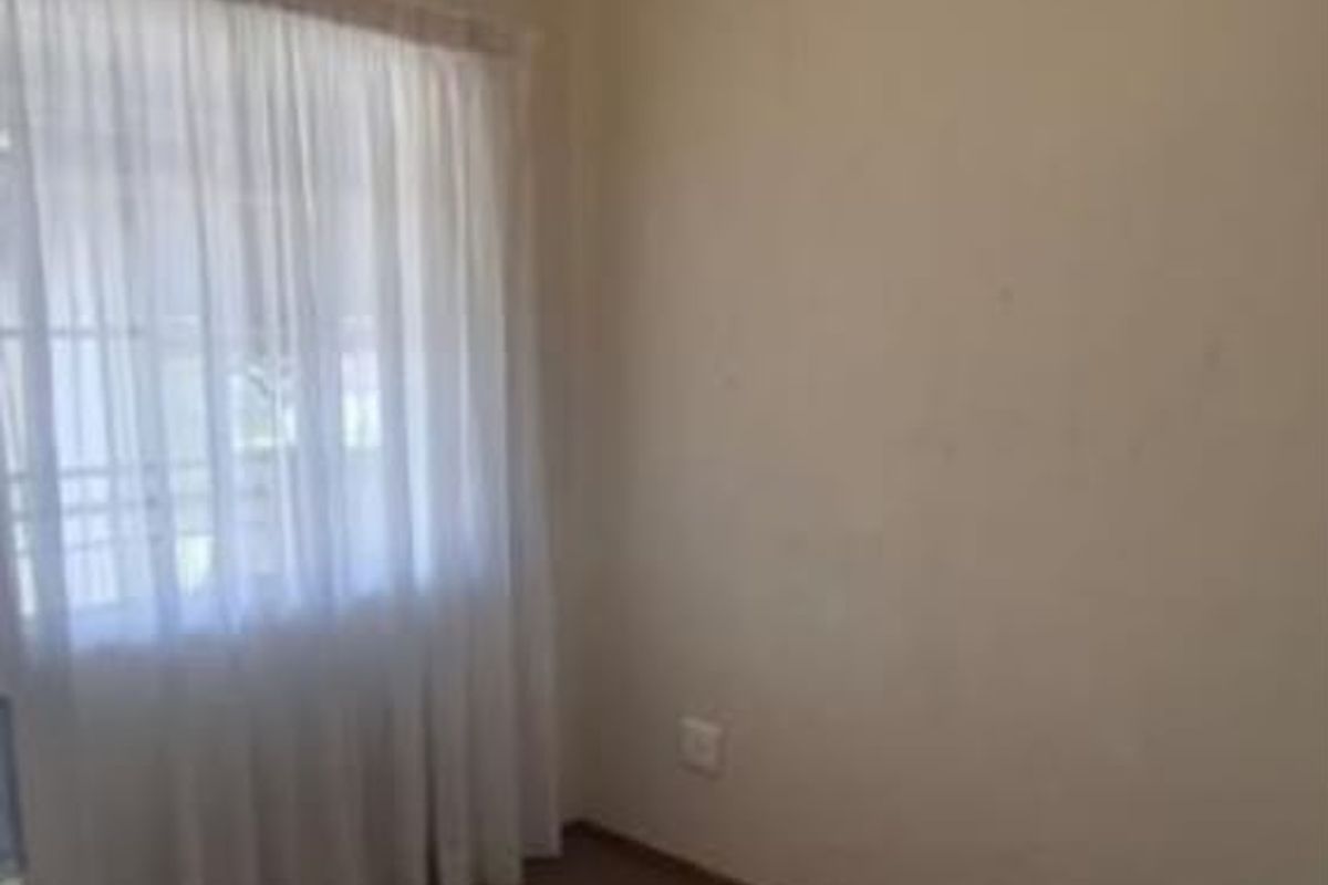 A compact, empty bedroom featuring neutral walls, carpeted flooring, and a window with installed curtain rails.