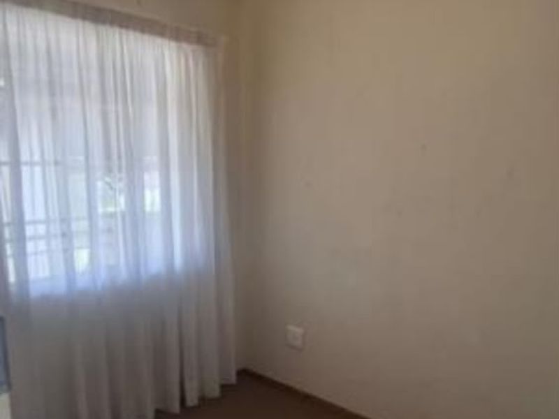 A compact, empty bedroom featuring neutral walls, carpeted flooring, and a window with installed curtain rails.