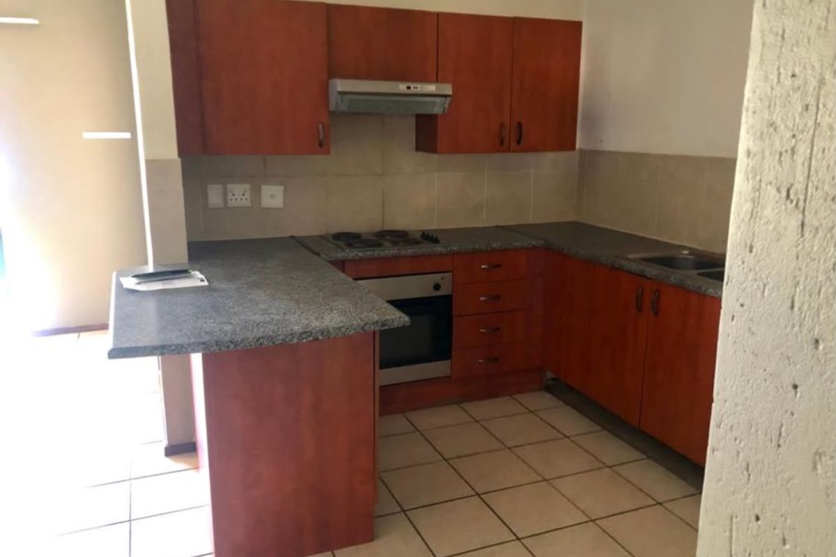 A functional kitchen featuring wood-finish cabinetry, granite-look laminate countertops, a built-in oven with hob, and tiled flooring throughout.