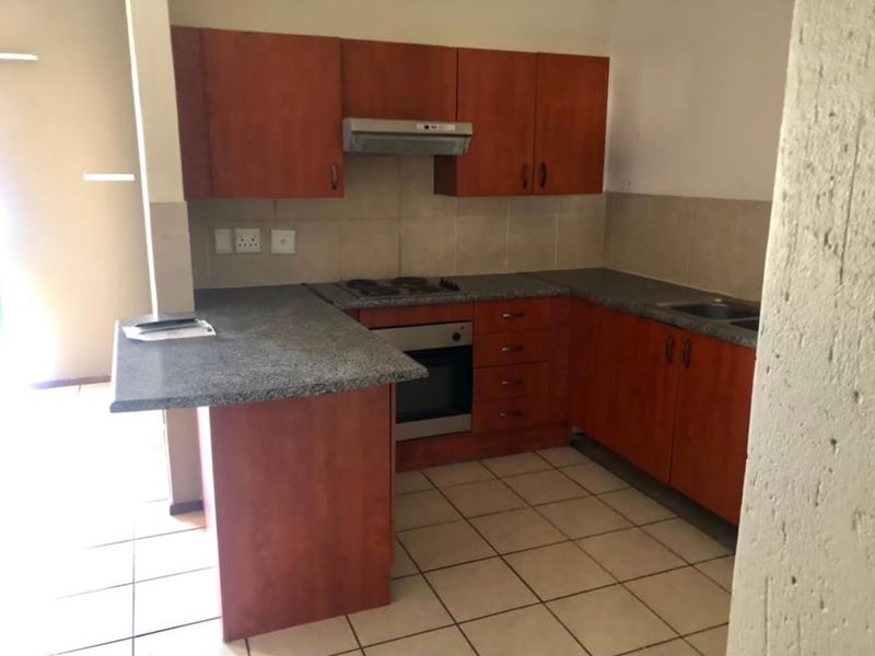 A functional kitchen featuring wood-finish cabinetry, granite-look laminate countertops, a built-in oven with hob, and tiled flooring throughout.