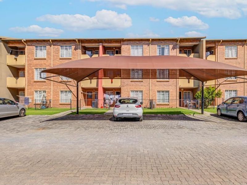Exterior view of an apartment complex featuring a brick facade and a covered parking area with shade cloth structure.