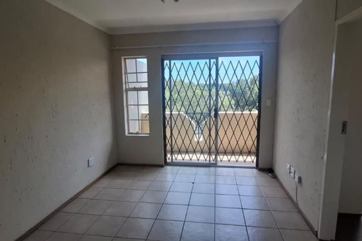 An empty living room featuring tiled flooring and a sliding glass door with a security gate, providing access to an outdoor balcony area.