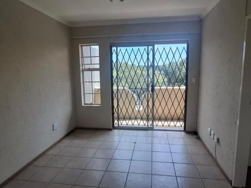 An empty living room featuring tiled flooring and a sliding glass door with a security gate, providing access to an outdoor balcony area.