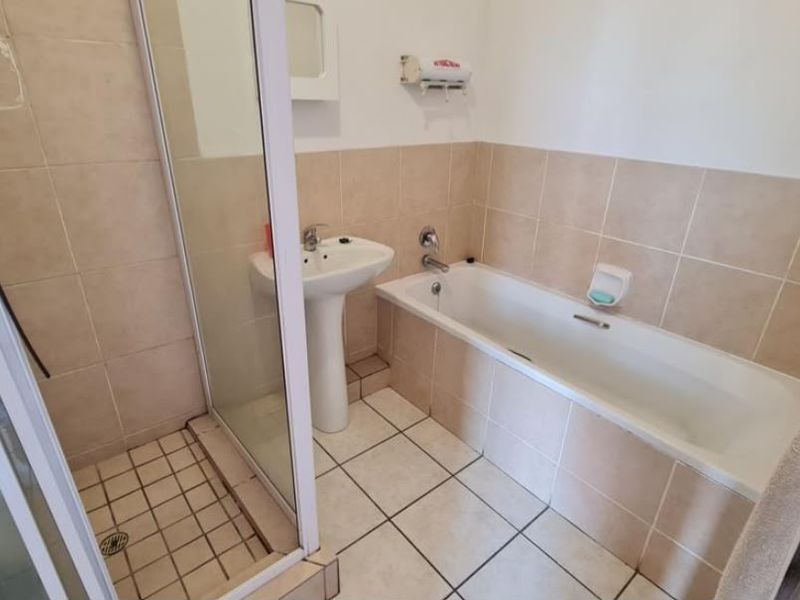 A functional bathroom featuring a separate shower enclosure, a bathtub, and a pedestal basin with neutral wall and floor tiling.