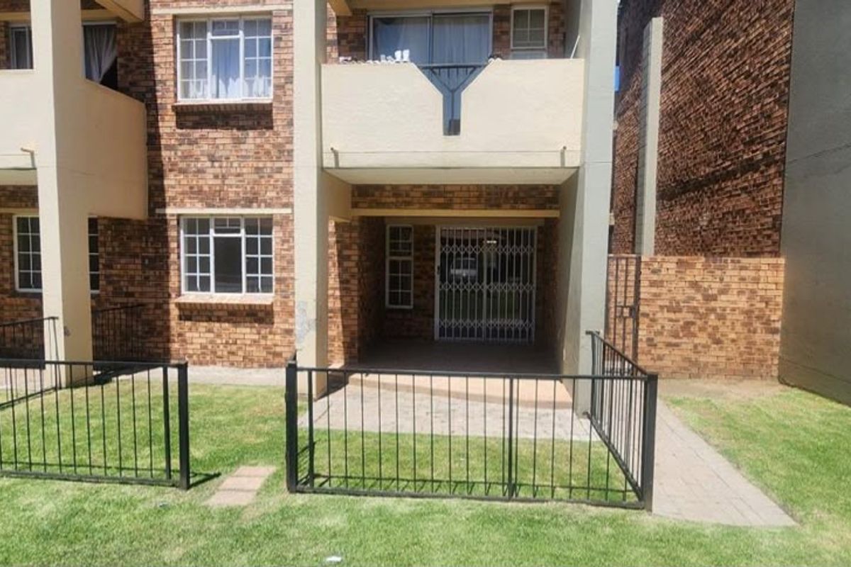Rear view of a face brick apartment building featuring a ground floor patio with security gate and an upper level balcony.