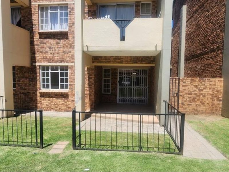 Rear view of a face brick apartment building featuring a ground floor patio with security gate and an upper level balcony.