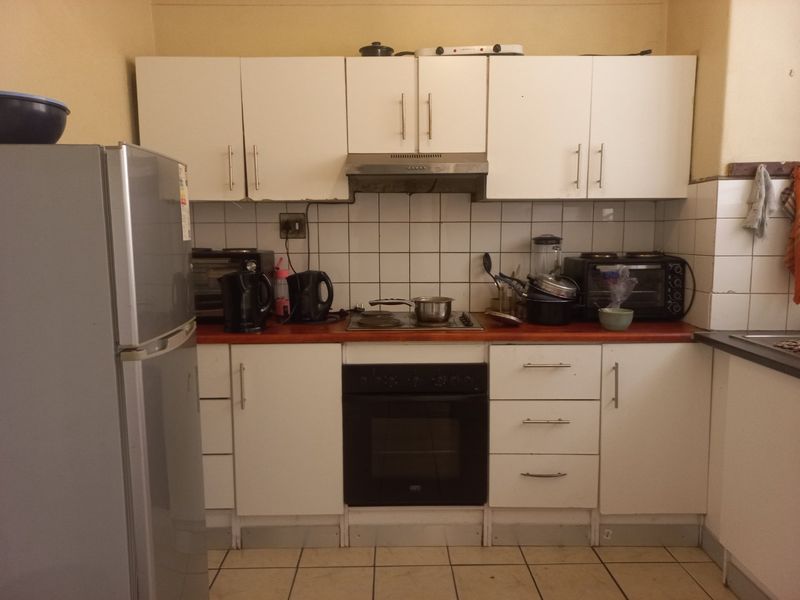 A functional kitchen featuring white built-in cabinetry, a tiled backsplash, an integrated oven, and a hob with an extractor fan.