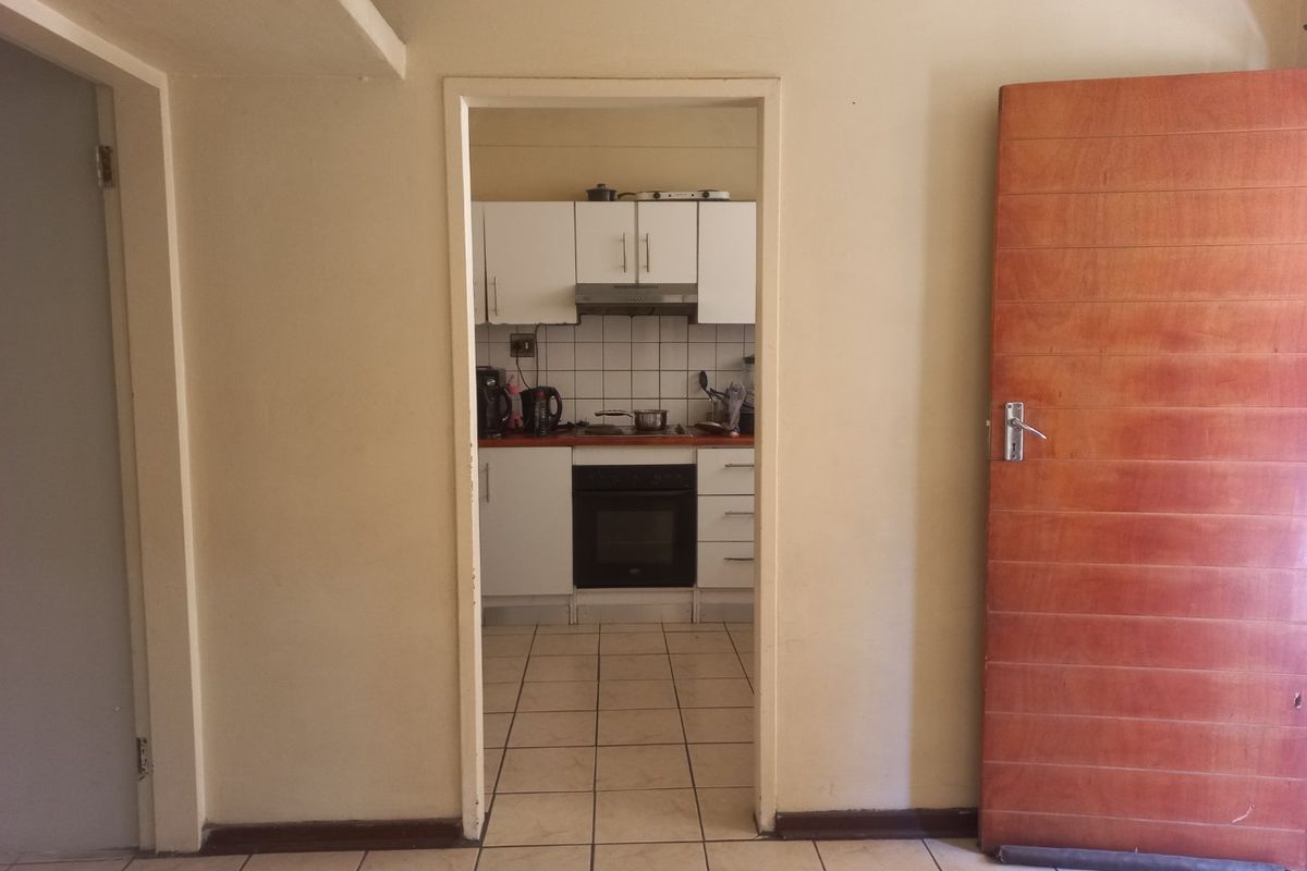 A view through a doorway into a functional kitchen featuring white cabinetry, tiled backsplash, built-in oven, and hob with tiled flooring throughout.